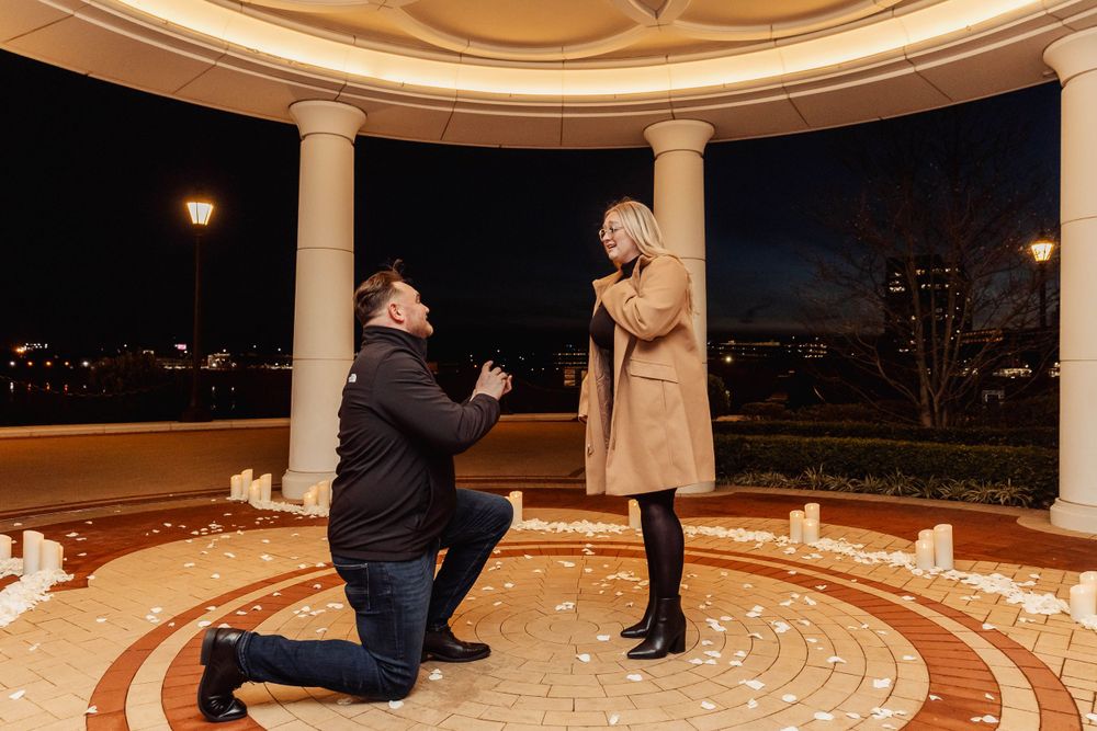 A proposal moment captured in a beautiful gazebo setting at night with city lights in the background.