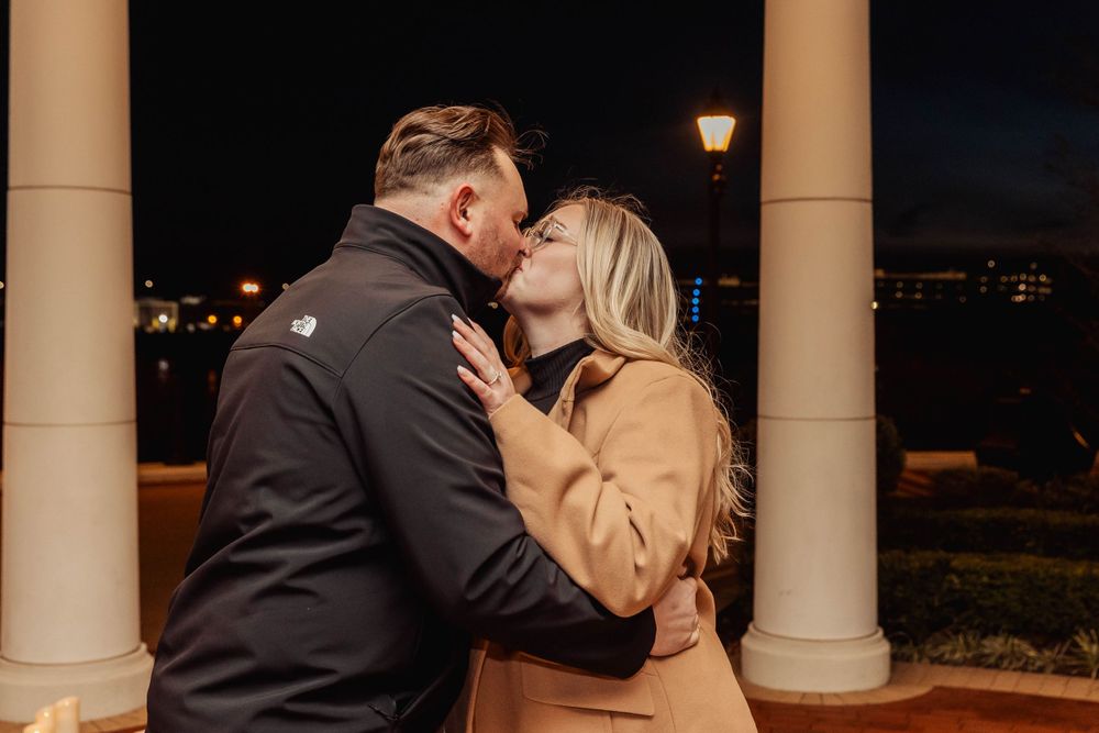 A romantic embrace under a columned structure with nighttime city views.