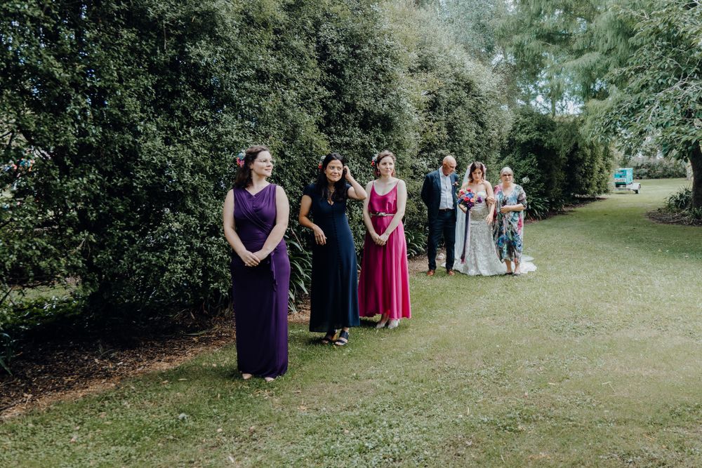 Wedding attendants in vibrant purple and pink dresses standing in a garden setting.