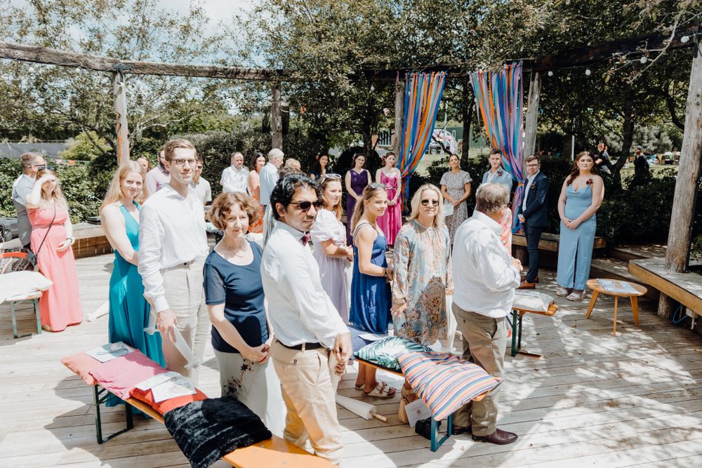 Guests enjoying an outdoor wedding celebration under trees with festive decorations.