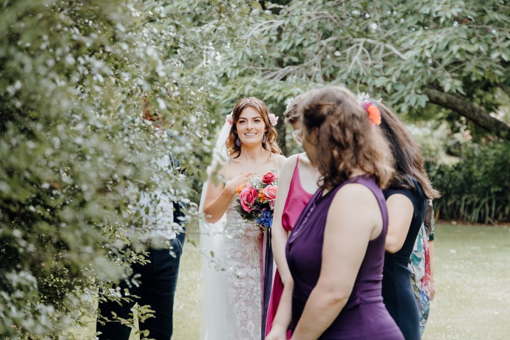 A garden wedding scene with attendants in purple and pink dresses holding bright bouquets.
