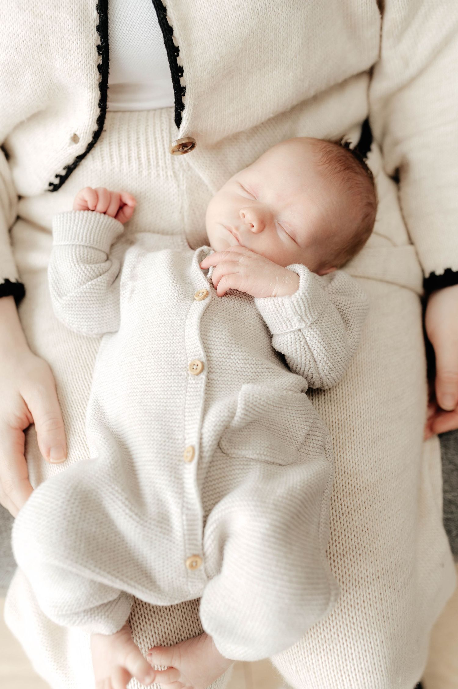 A sleeping baby wearing a cozy cream-colored knit romper lies peacefully on soft fabric.