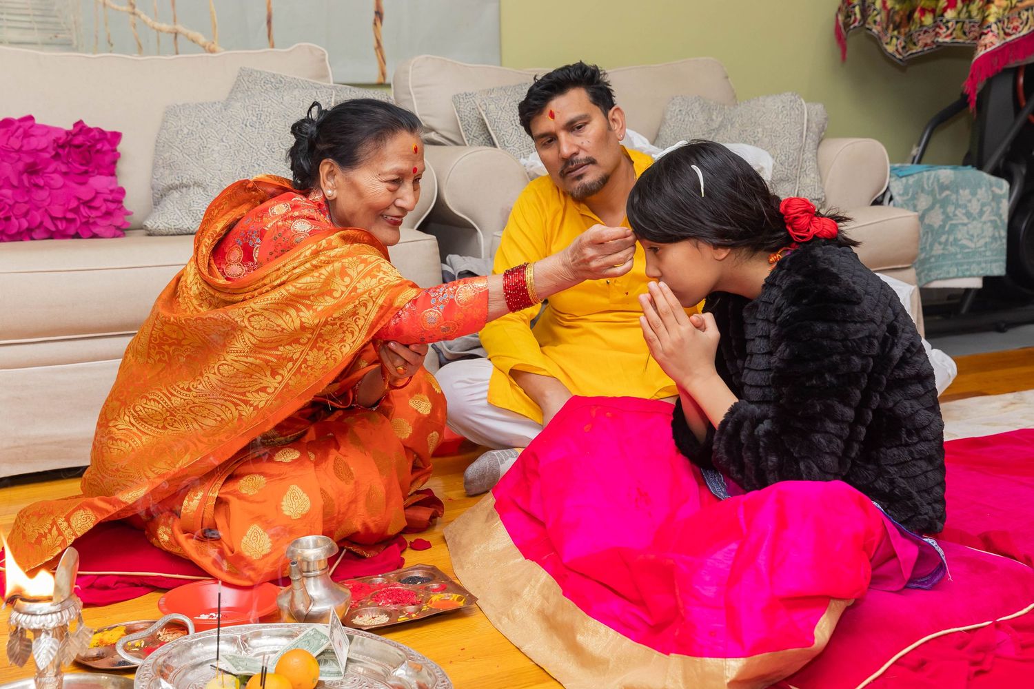 Traditional ceremony with people in vibrant orange and pink attire sharing a ritual moment.