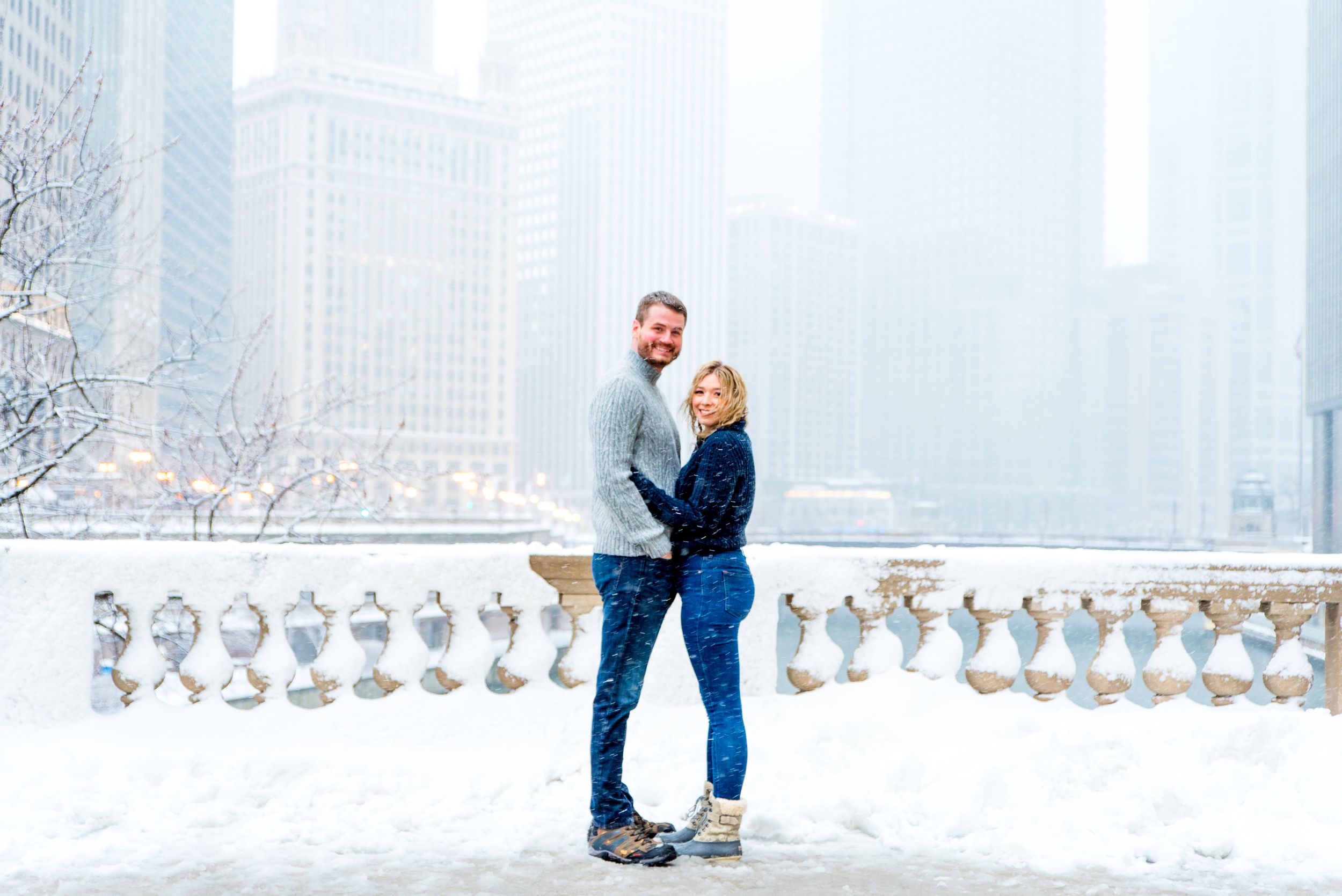 couple hugging in the snow at Wrigley Building overlooking the Chicago River for snowy winter engagement pictures