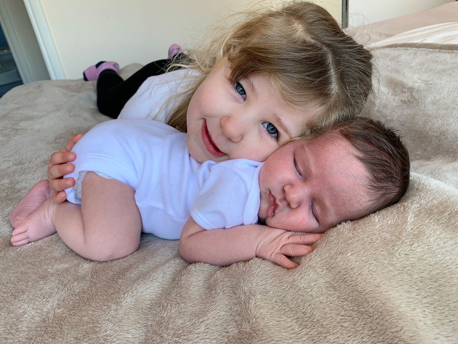 a toddler girl smiles while resting her head on her newborn baby sister during a photoshoot in didcot