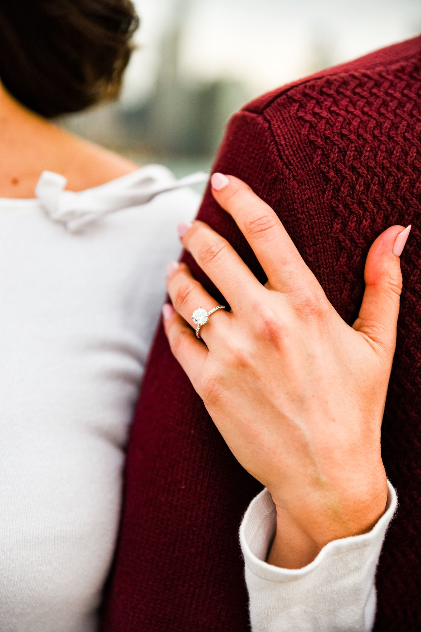 woman's hand with engagement ring wrapped around man's arm in red sweater