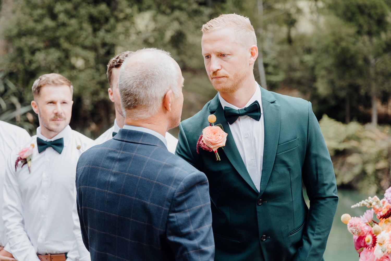 Wedding ceremony participants in formal attire stand together during outdoor service.