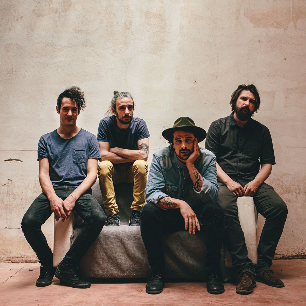 Four casual dressed people sitting together on a stone ledge against a beige wall.