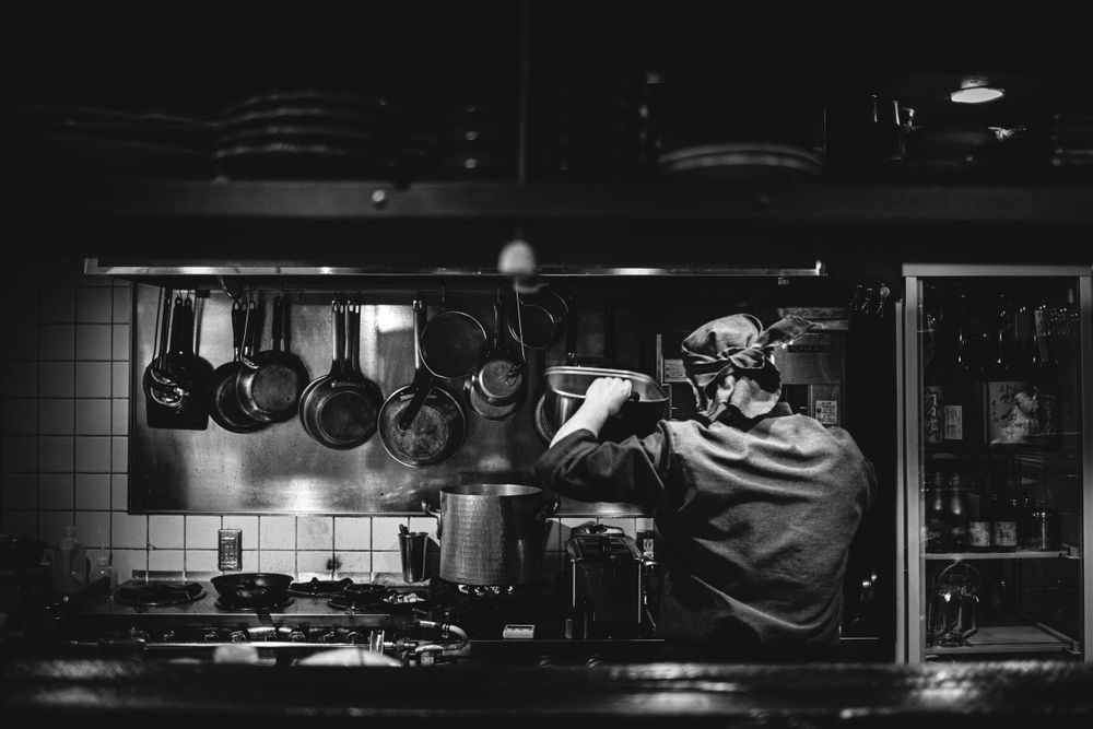 Kitchen scene with hanging pots and pans silhouetted against dim lighting.