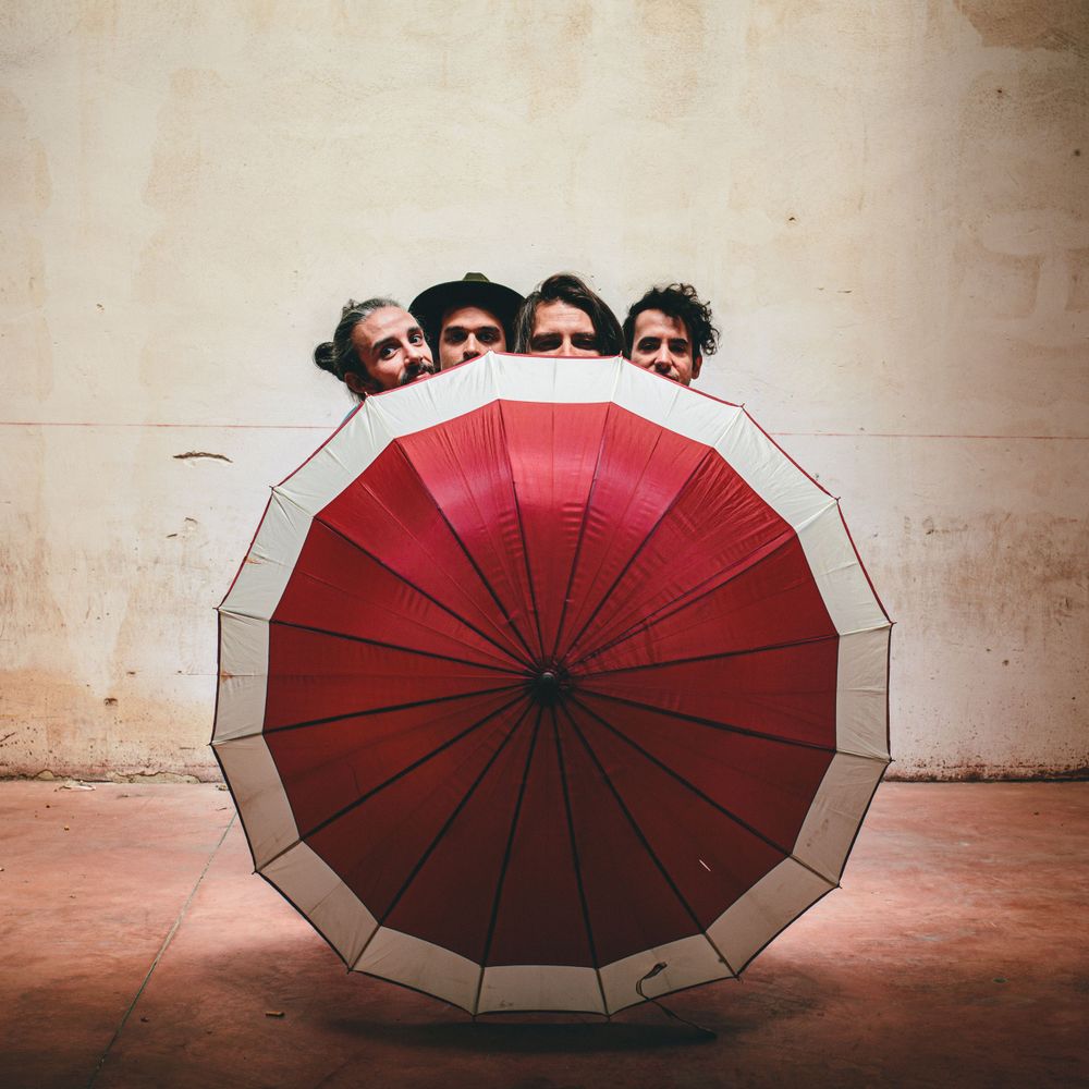 Creative photo of people peeking over a red and white umbrella against a light colored wall.