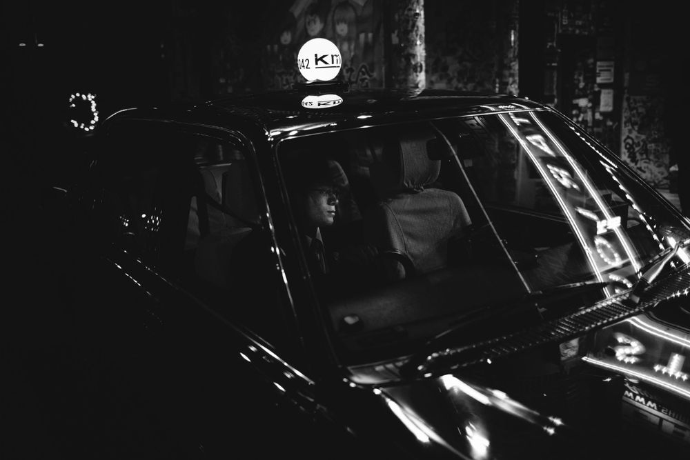 Black and white image of a taxi at night with illuminated signage.