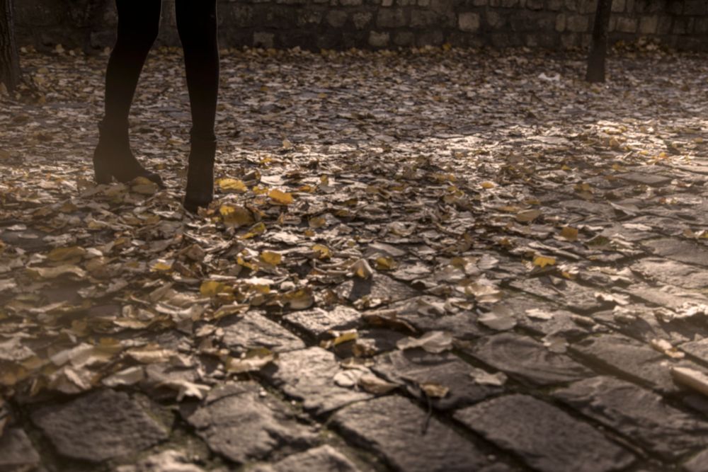 Low angle shot of feet walking on cobblestone street covered in autumn leaves.