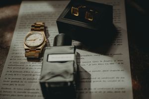 Wedding accessories including gold watch, cufflinks box and rings arranged on document.