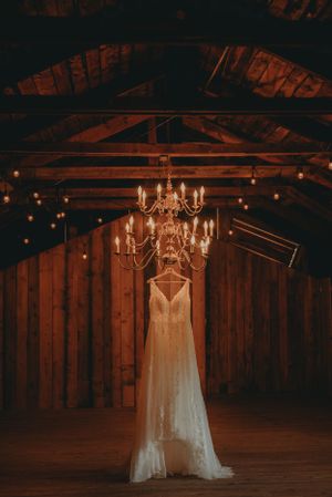 An elegant white wedding dress hangs from rustic wooden beams under a crystal chandelier.
