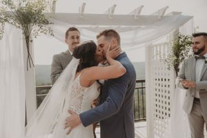 Romantic first kiss moment under white pergola at outdoor wedding ceremony.