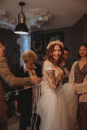 A bride in a white lace dress with tattoos getting ready during final wedding preparations.