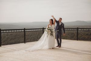 Newlyweds celebrating on deck overlooking mountain landscape in formal attire.