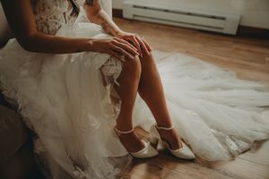 Close-up of elegant white wedding shoes and tulle dress on hardwood floor.