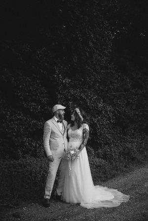 A black and white portrait of newlyweds standing against a textured wall outdoors.