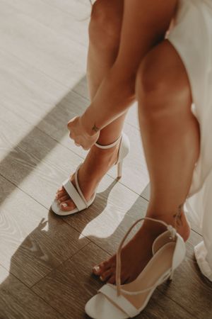 Close-up of white strappy wedding heels on wooden floor.