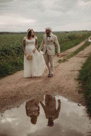 A rustic wedding photo with the couple's reflection captured in a puddle on a dirt path.