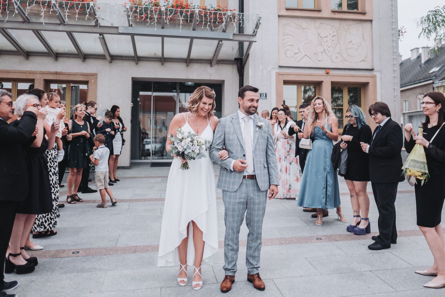 Wedding guests cheer as newlyweds exit ceremony venue together.