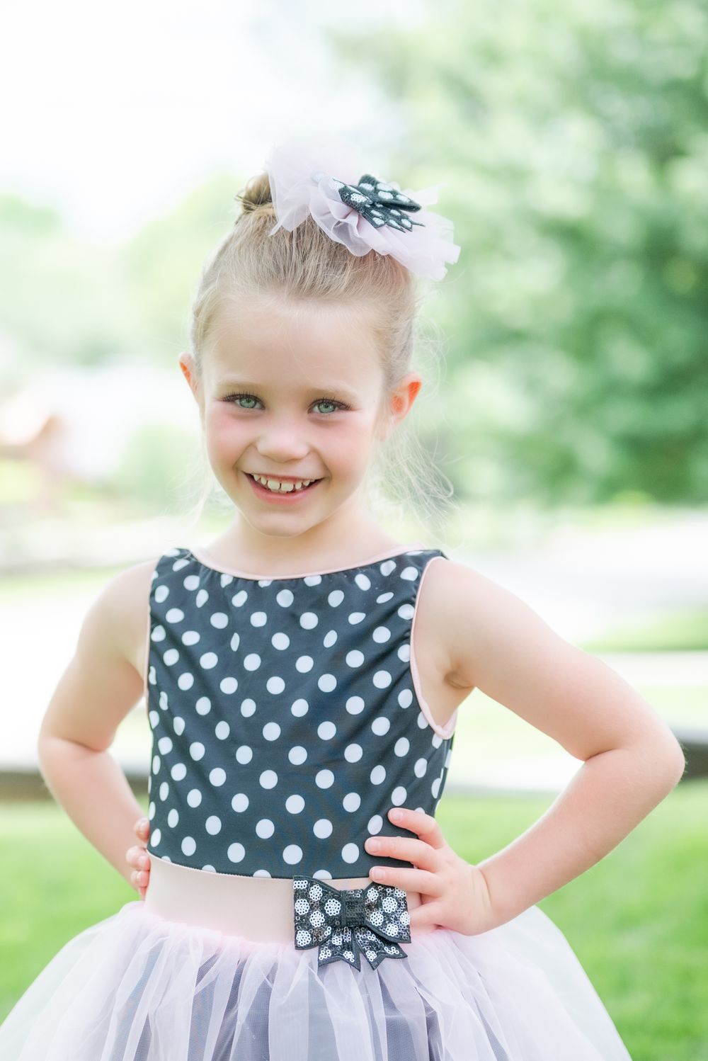 Young girl in polka dot dress and tulle skirt poses with hand on hip outdoors.