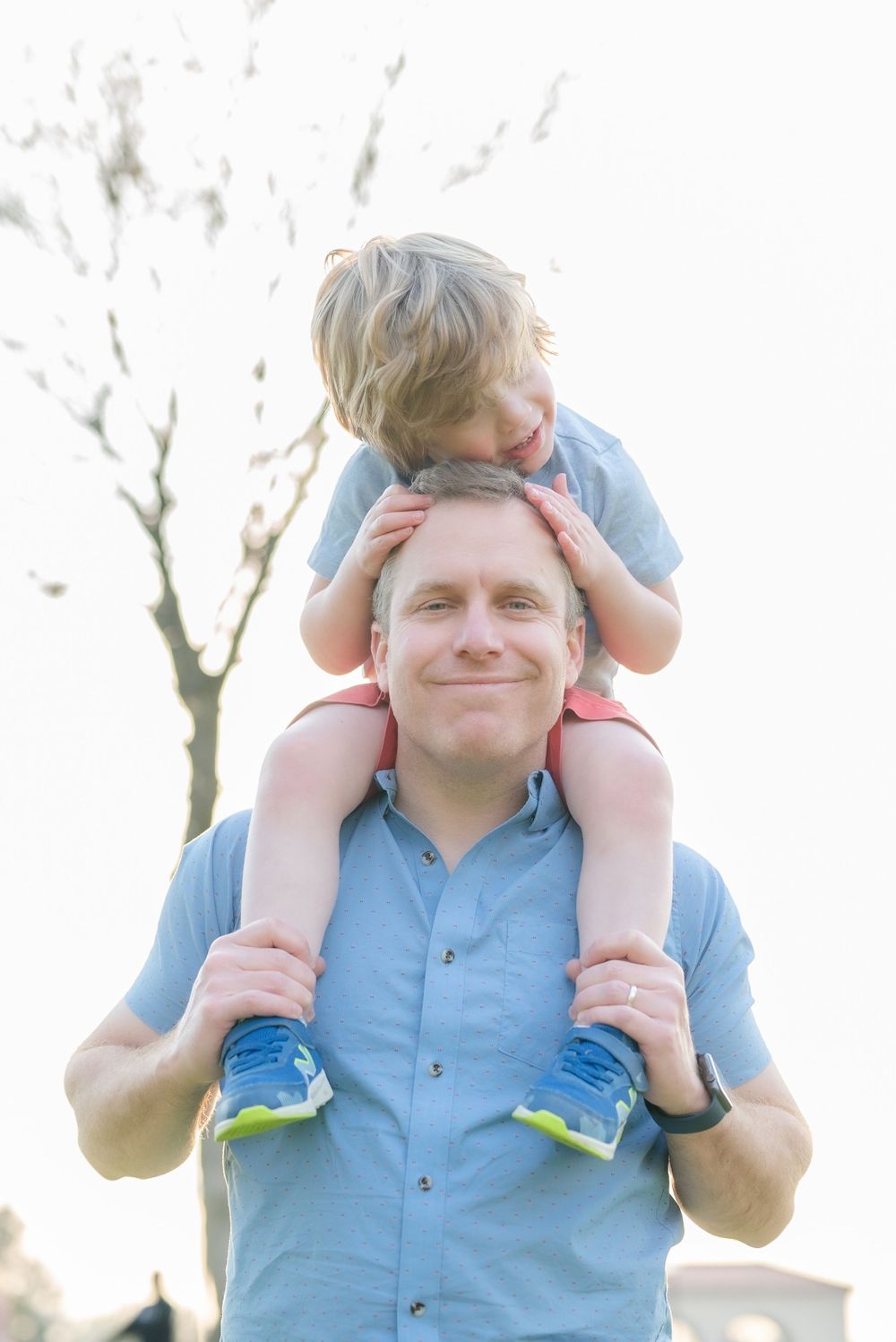 Playful shoulder ride scene between parent and child against bright sky.