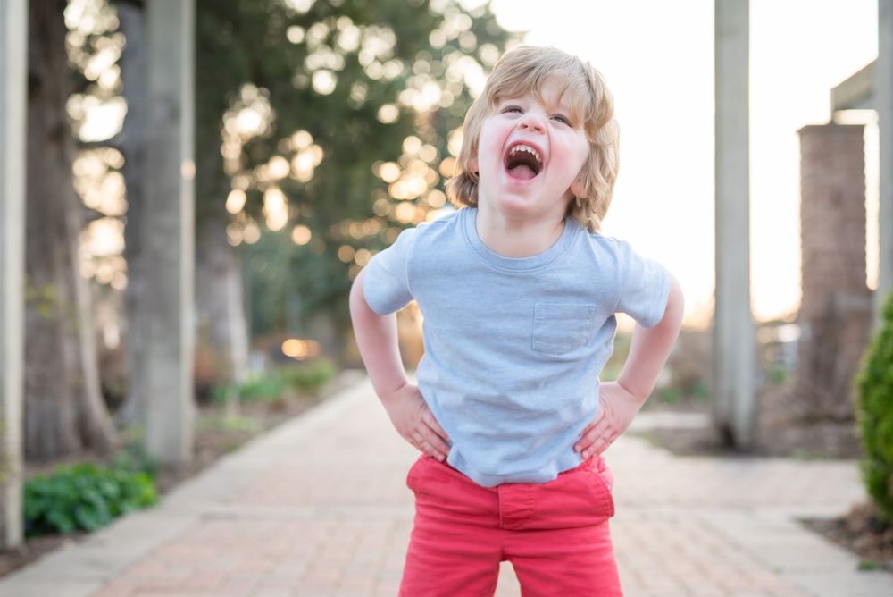 Joyful child in blue shirt and red pants laughs expressively on outdoor path.