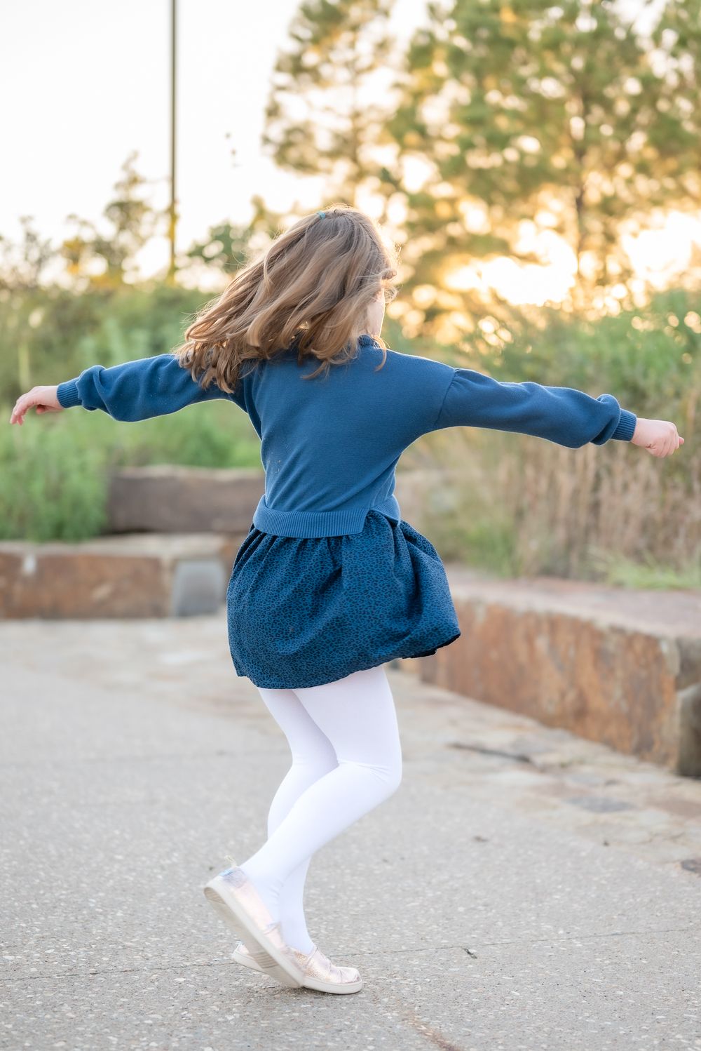 Child twirling in navy blue dress and white tights against sunset background.