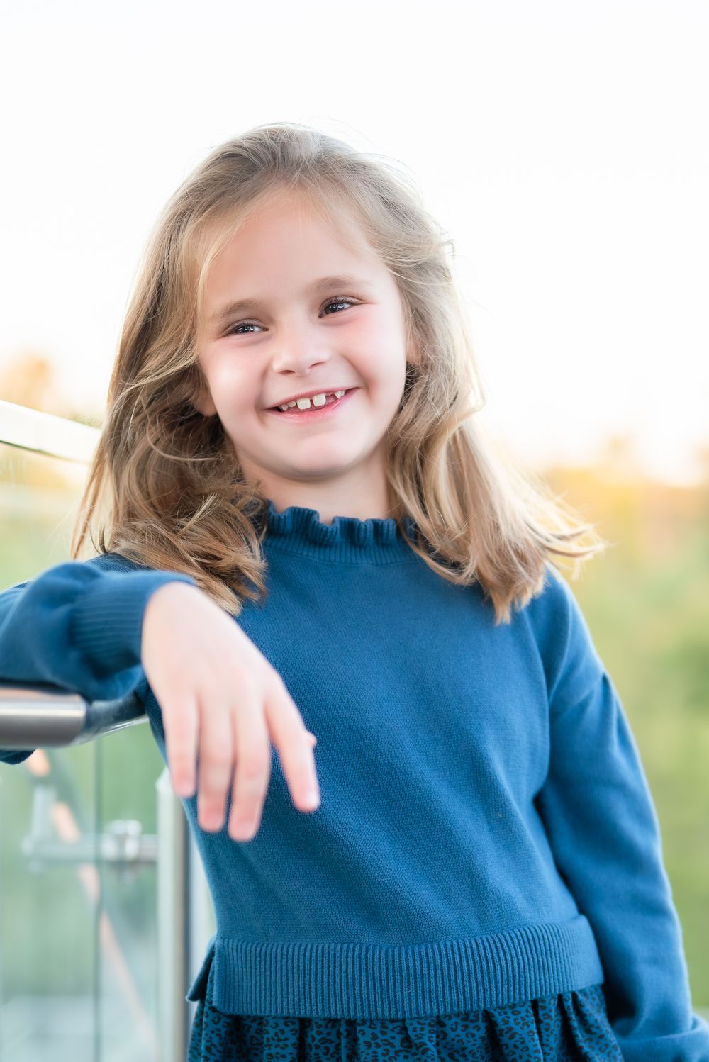Child in navy sweater leans casually against railing in outdoor portrait.
