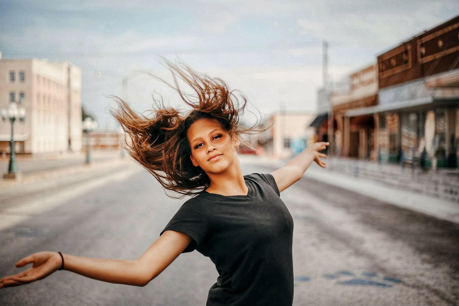 Young woman with windswept hair dancing on an empty street at sunset.