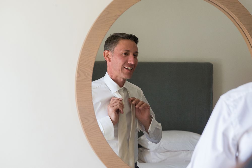 groom fixes his tie in front of the mirror at his preparation before the wedding