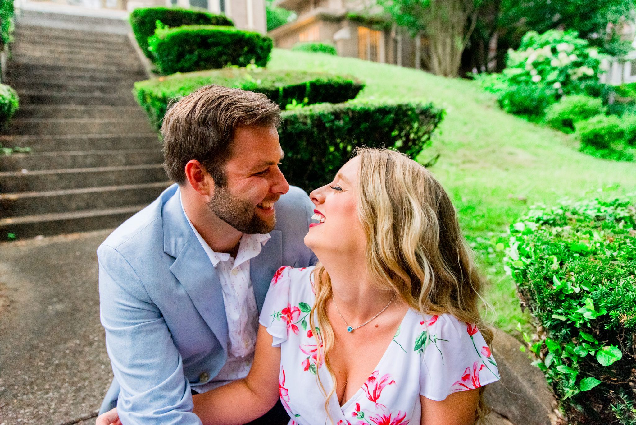 engaged couples in floral dress and light blue suit jacket and jeans sitting on staircase on a rainy day
