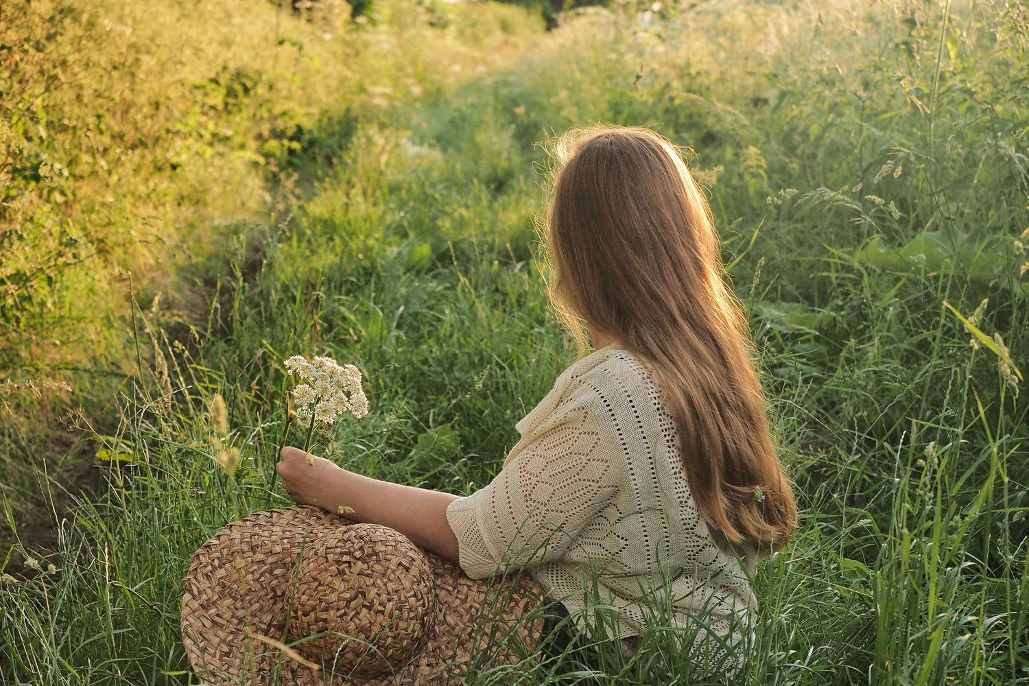 A girl sits in the long grass enjoying the last rays of evening sun