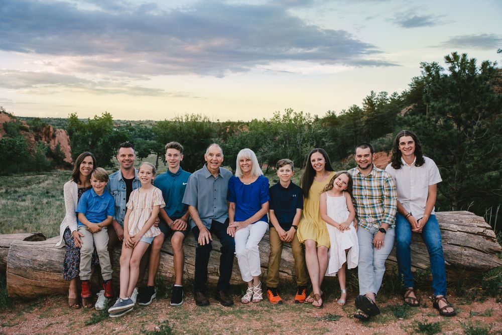 And extended family group sits on a log to pose for a portrait with a forest background.