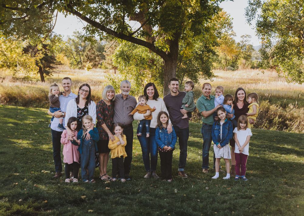 An extended family group poses in a grassy field with trees in the background.