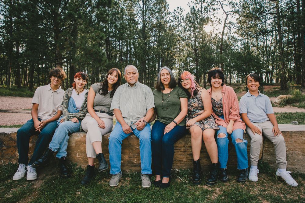 An extended family group with grandparents sits together on a group of rocks.