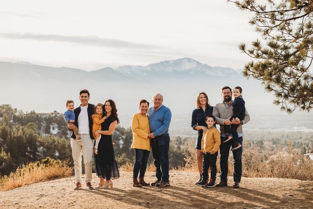 An extended family group stands in the sunlight on a clifftop with a snowy Pikes Peak in the background at Palmer Park