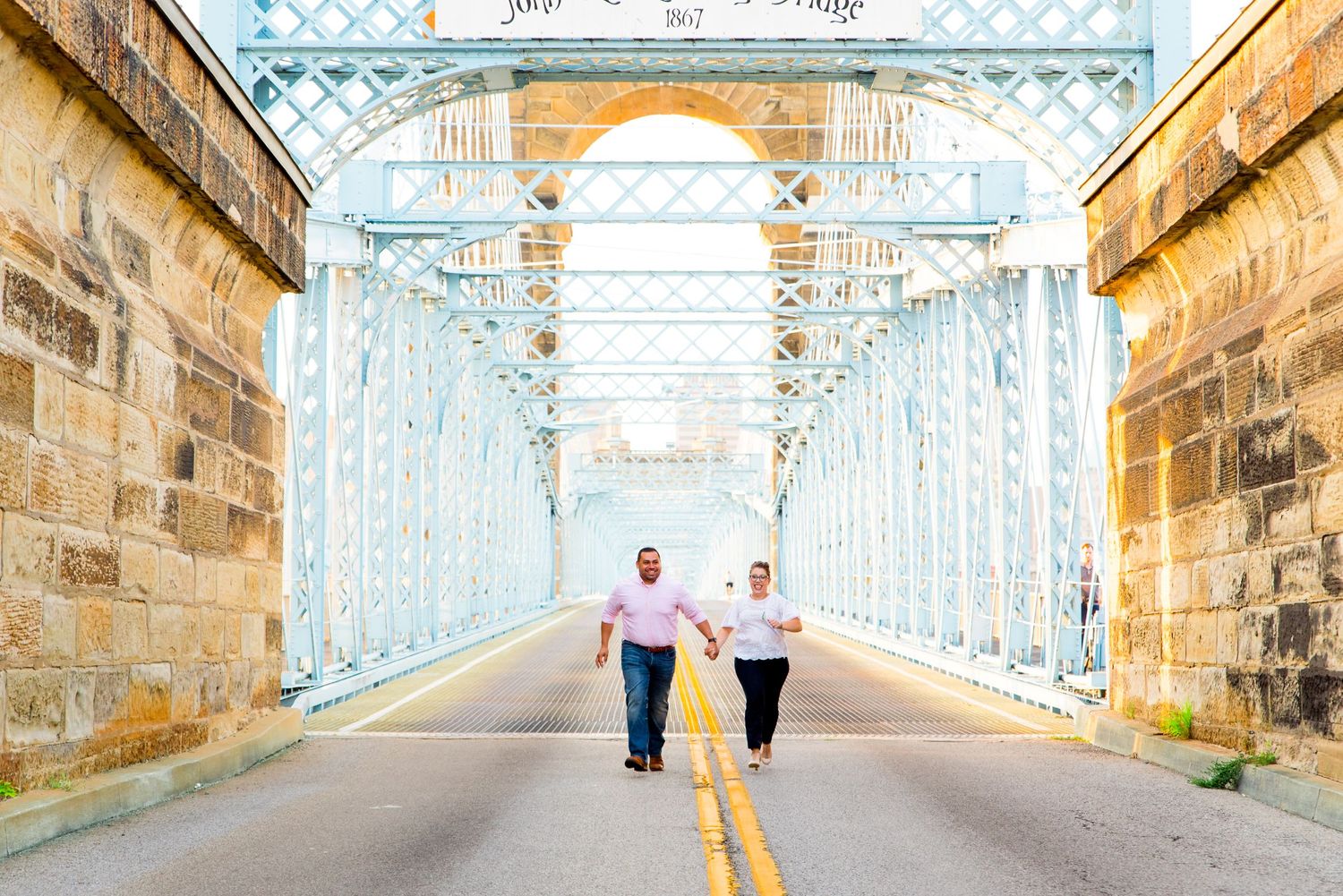 engaged couple holding hands and running through Roebling Bridge in downtown Cincinnati