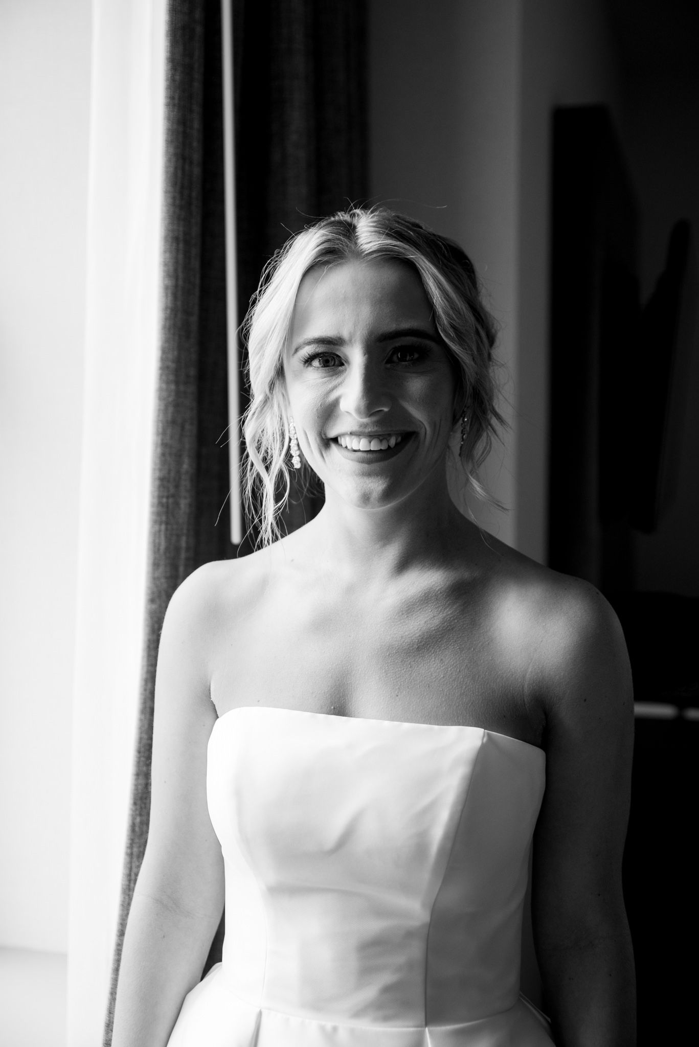 blonde bride with updo and strapless wedding dress smiling while getting ready