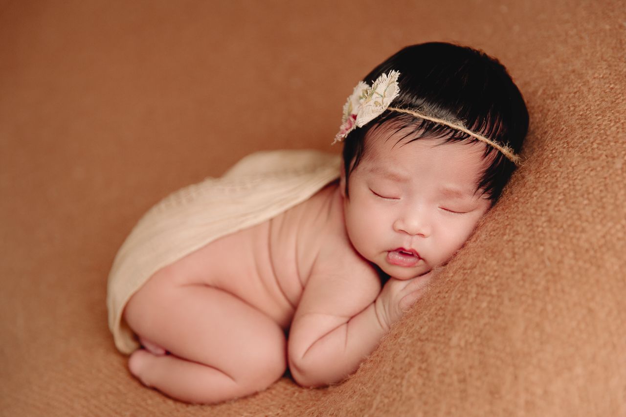 baby sleeping cuddled up on tummy on brown blanket rustic headband