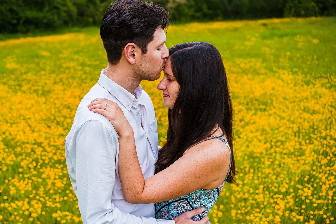man kissing partner on the forehead in a buttercup field