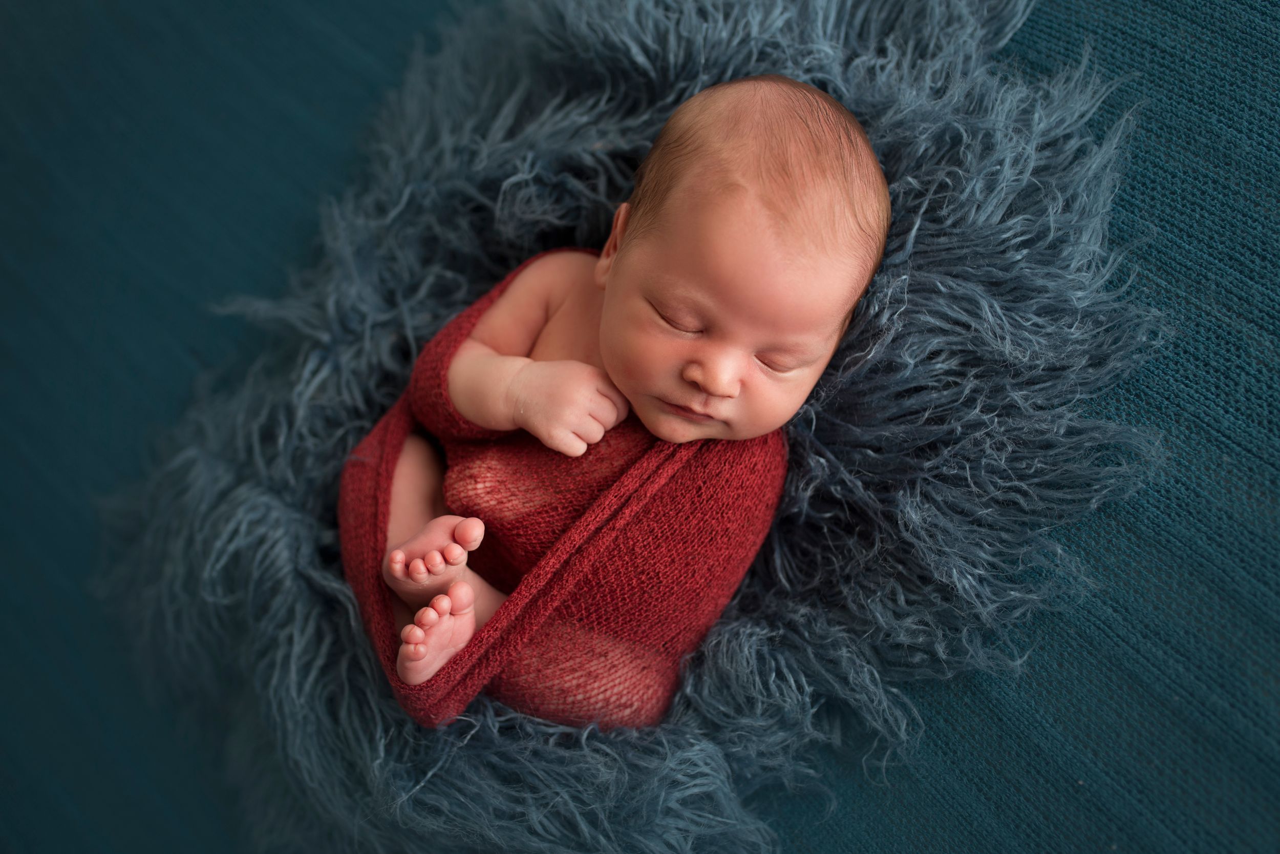 baby boy wrapped in red laying on blue fur
