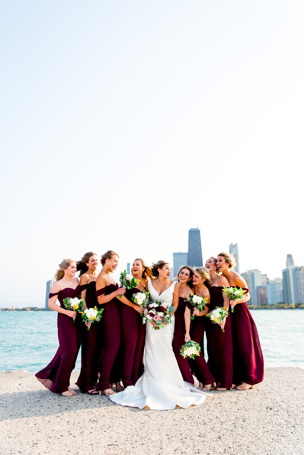 laughing bridesmaids in maroon take pictures with bride at north avenue beach pier