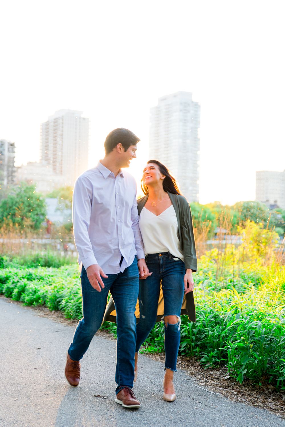 man and woman in jeans and army green jacket walking at sunset holding hands in Lincoln park