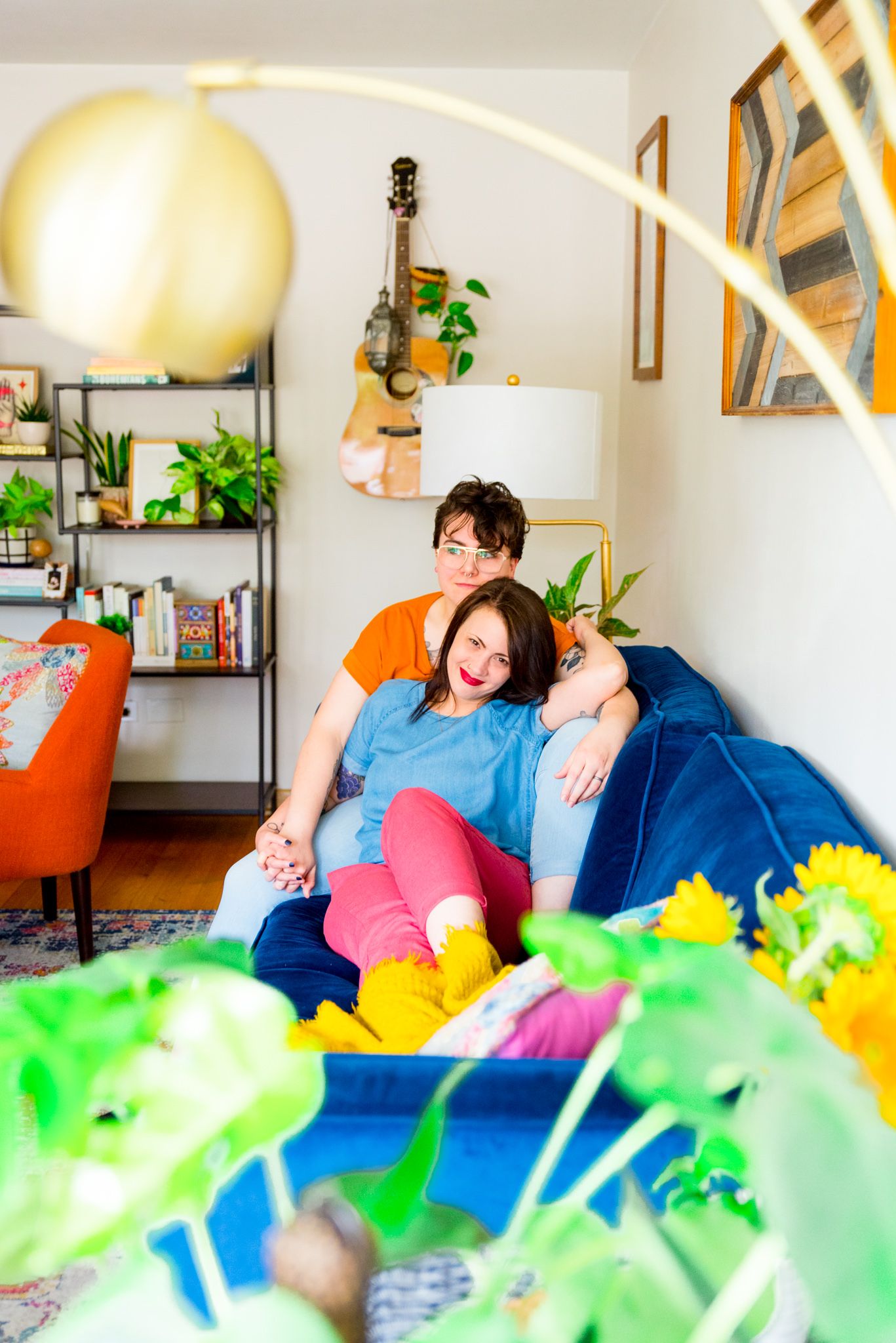 woman in blue shirt and pink pants sitting with wife in orange shirt on blue couch in colorful living room