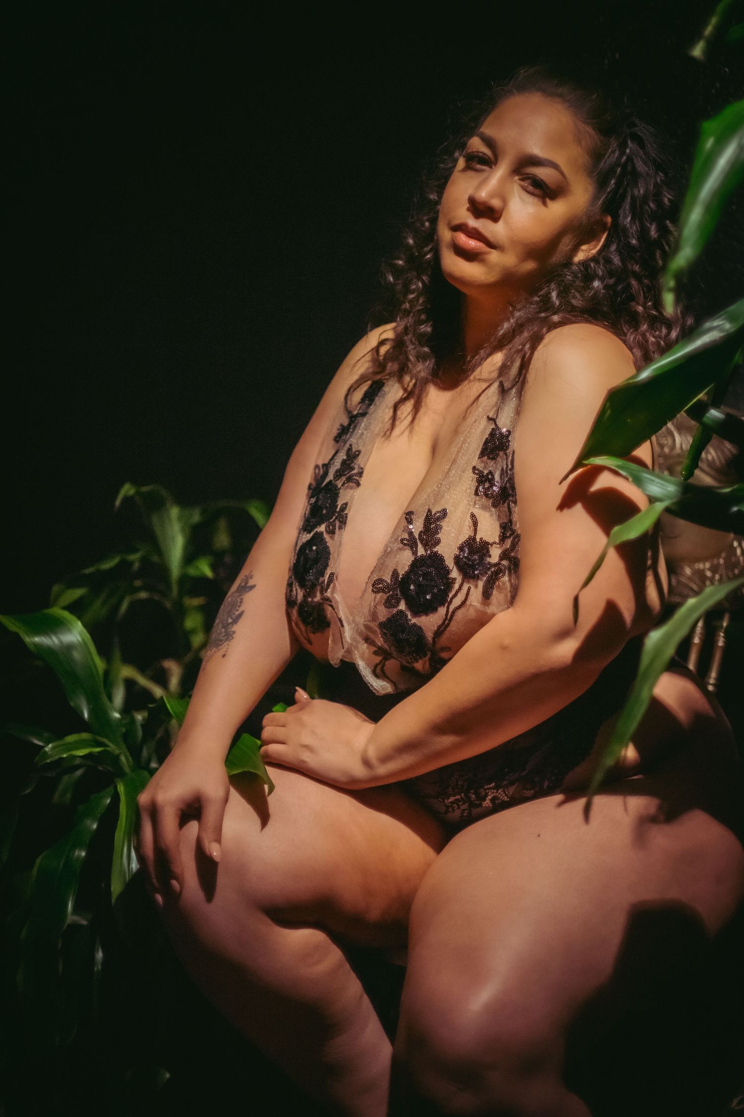Plus size woman in lingerie posing in lingerie againt wall with plant
