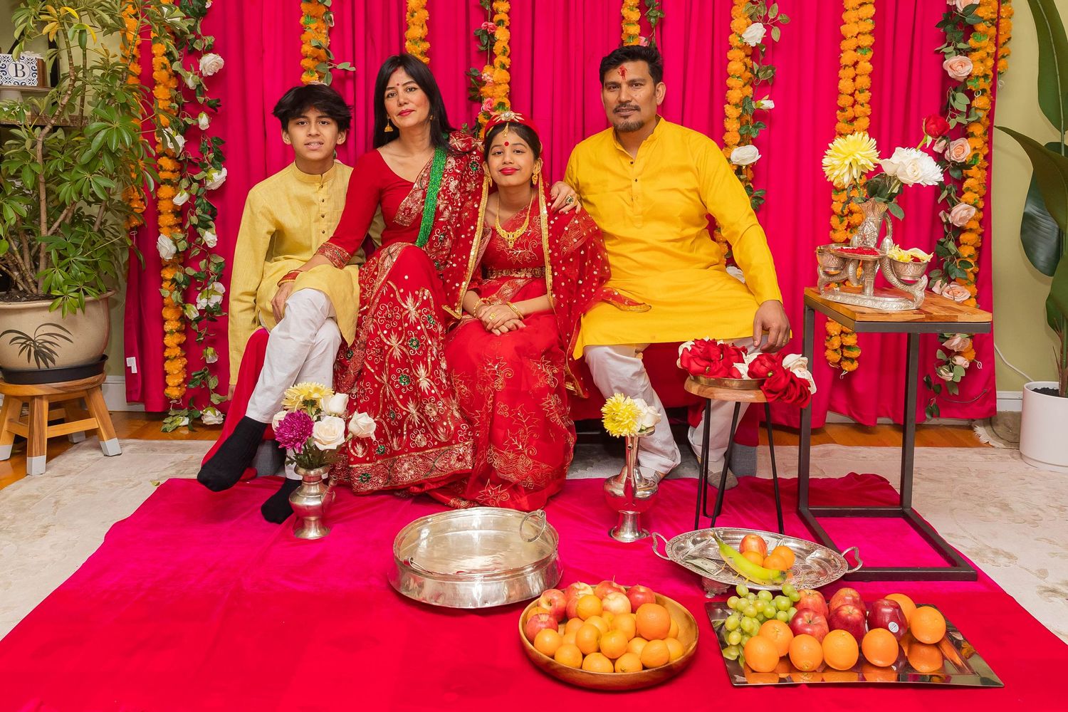 Traditional Hindu ceremony with family members in yellow and red attire seated with ceremonial food offerings.