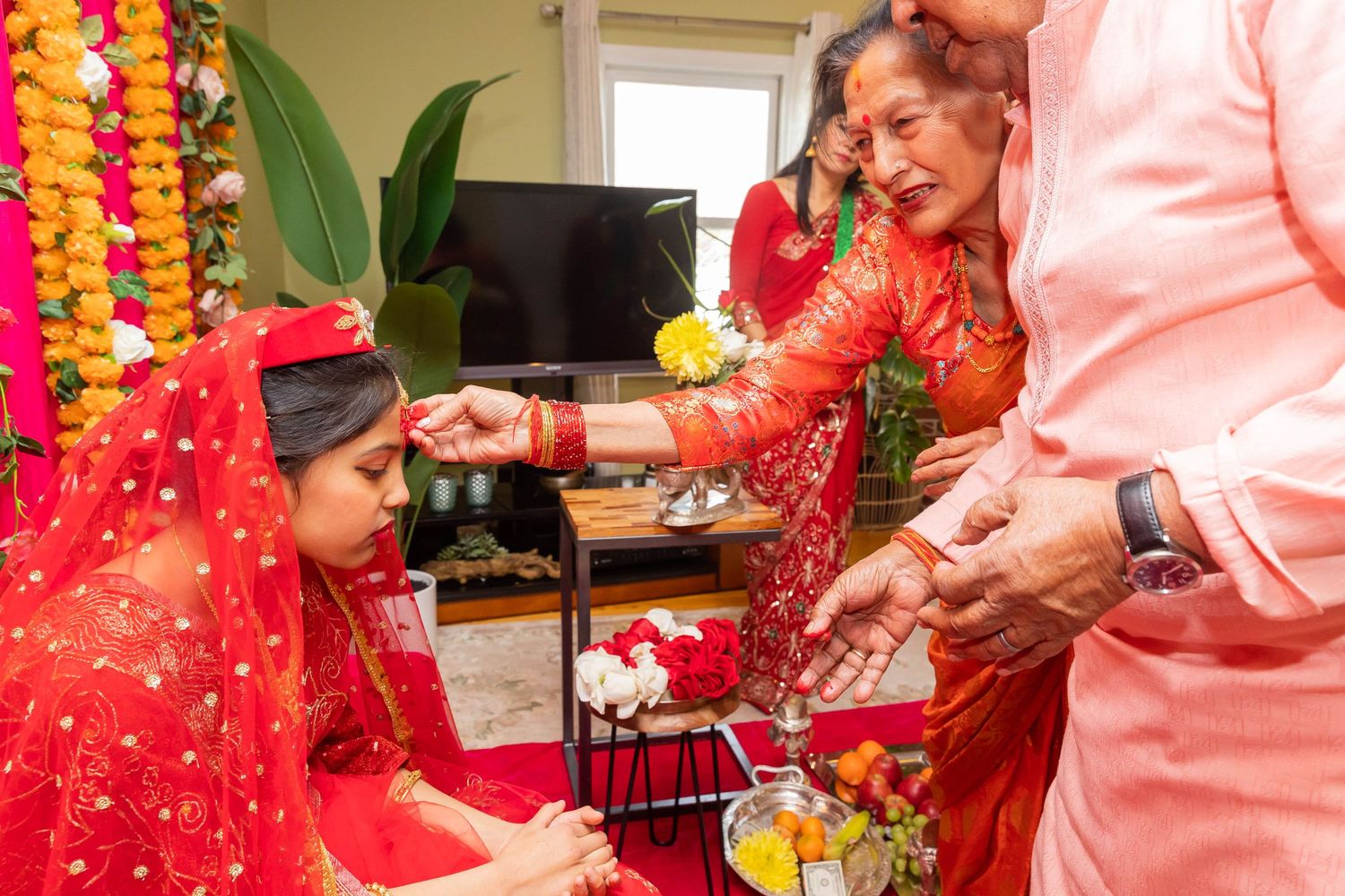 Traditional Hindu blessing ritual with participants in formal red and pink attire.